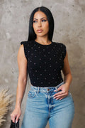 Woman wearing a black polka dot top and blue jeans against a gray concrete wall.