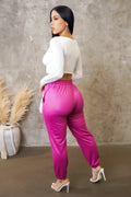 Woman wearing a white top and pink pants against a textured wall.