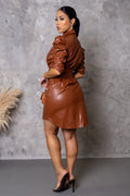 Woman wearing a brown leather outfit against a gray concrete wall.