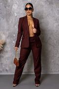 Woman in a burgundy suit holding a handbag against a gray background