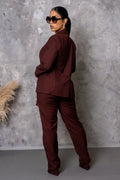 Woman in a burgundy suit standing against a gray textured wall.