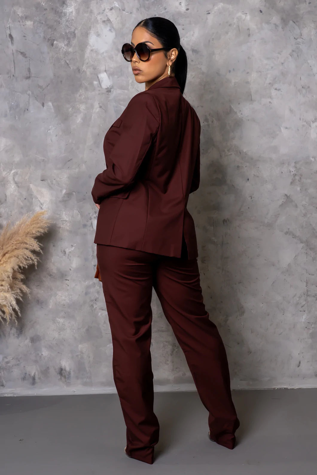 Woman in a burgundy suit standing against a gray textured wall.