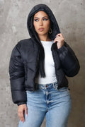 Woman wearing a black puffer jacket over a white top and blue jeans against a gray background