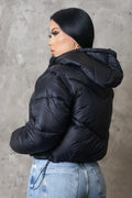 Person wearing a black puffer jacket against a gray concrete wall