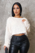 Woman wearing a white fuzzy sweater and black leather pants against a gray concrete wall.