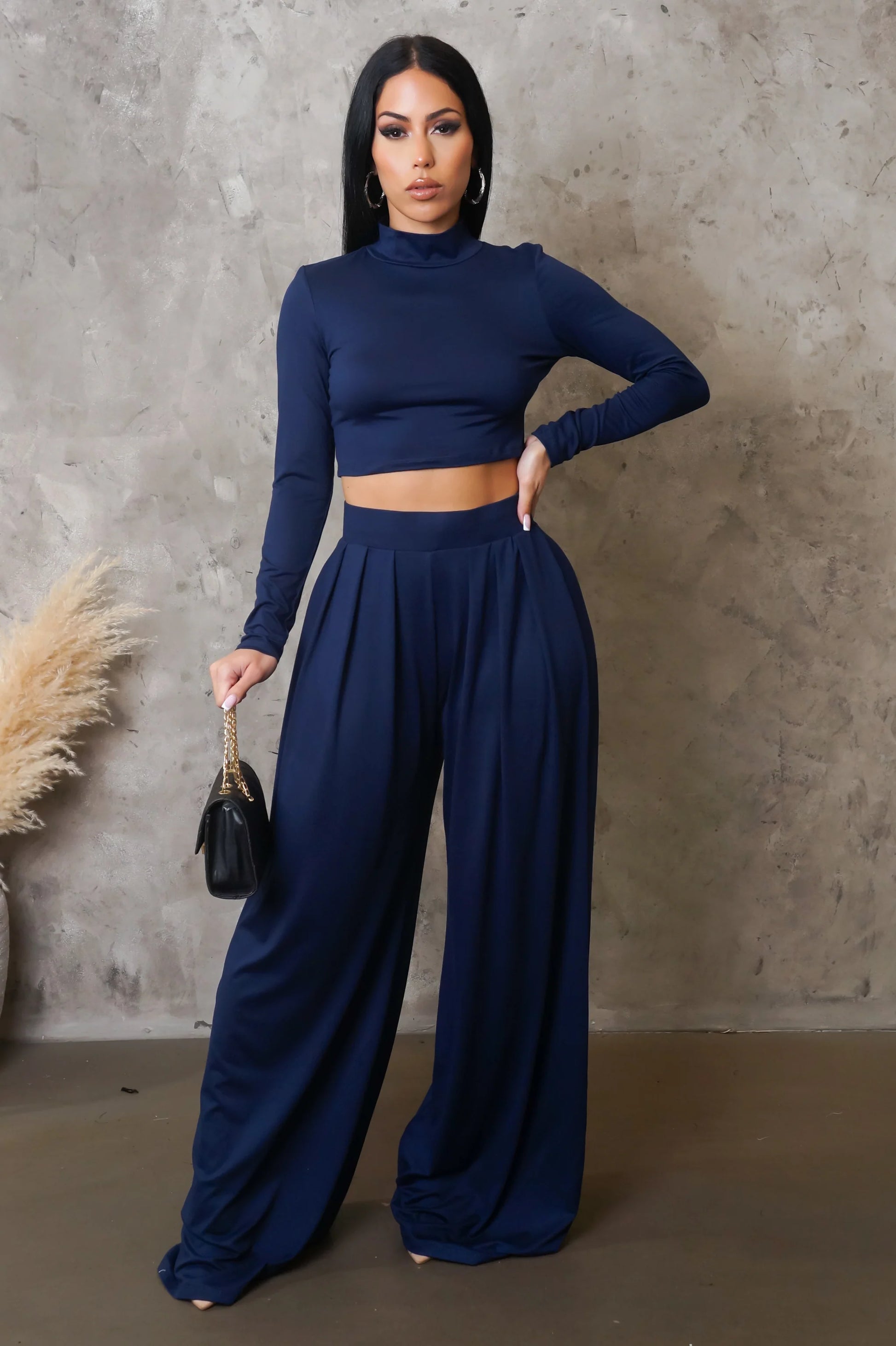 Woman wearing a navy blue outfit with wide-leg pants against a textured wall.

Details