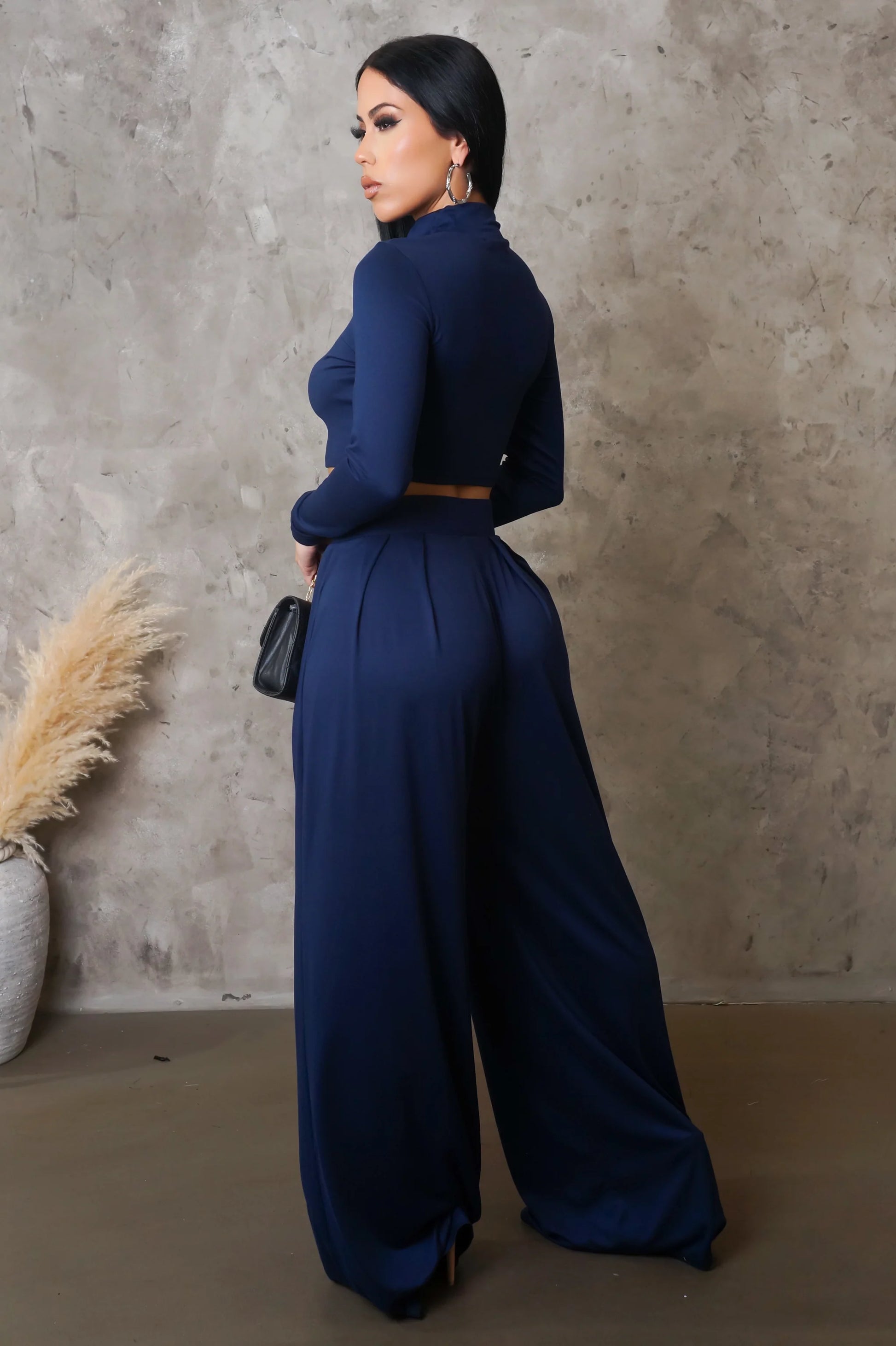 Woman wearing a navy blue jumpsuit against a textured wall.
