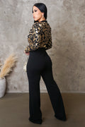 Woman wearing a leopard print top and black pants against a textured wall.