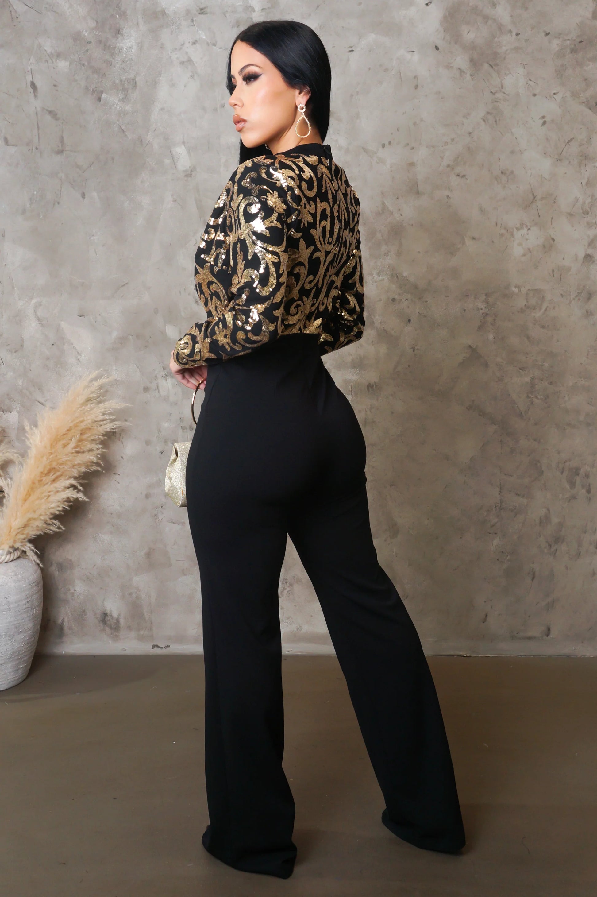 Woman wearing a leopard print top and black pants against a textured wall.