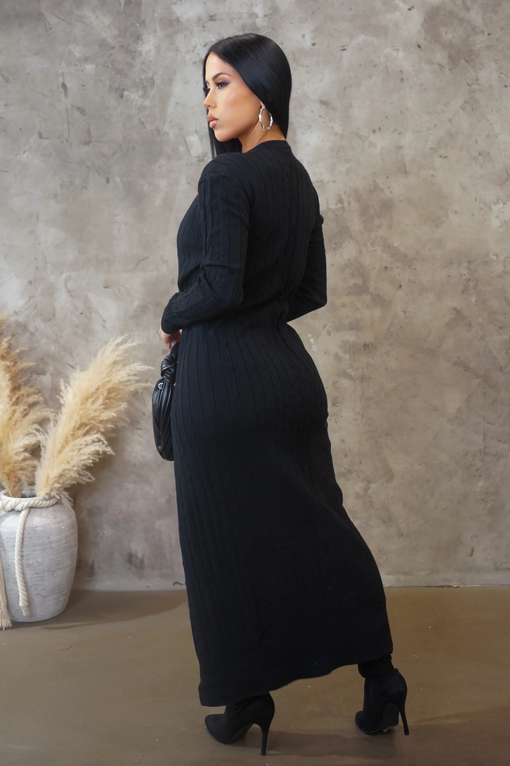 Woman in a black outfit standing against a textured wall with decorative elements.