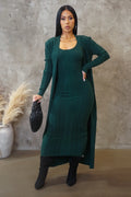 Woman wearing a green dress and cardigan set with a black handbag against a textured wall.