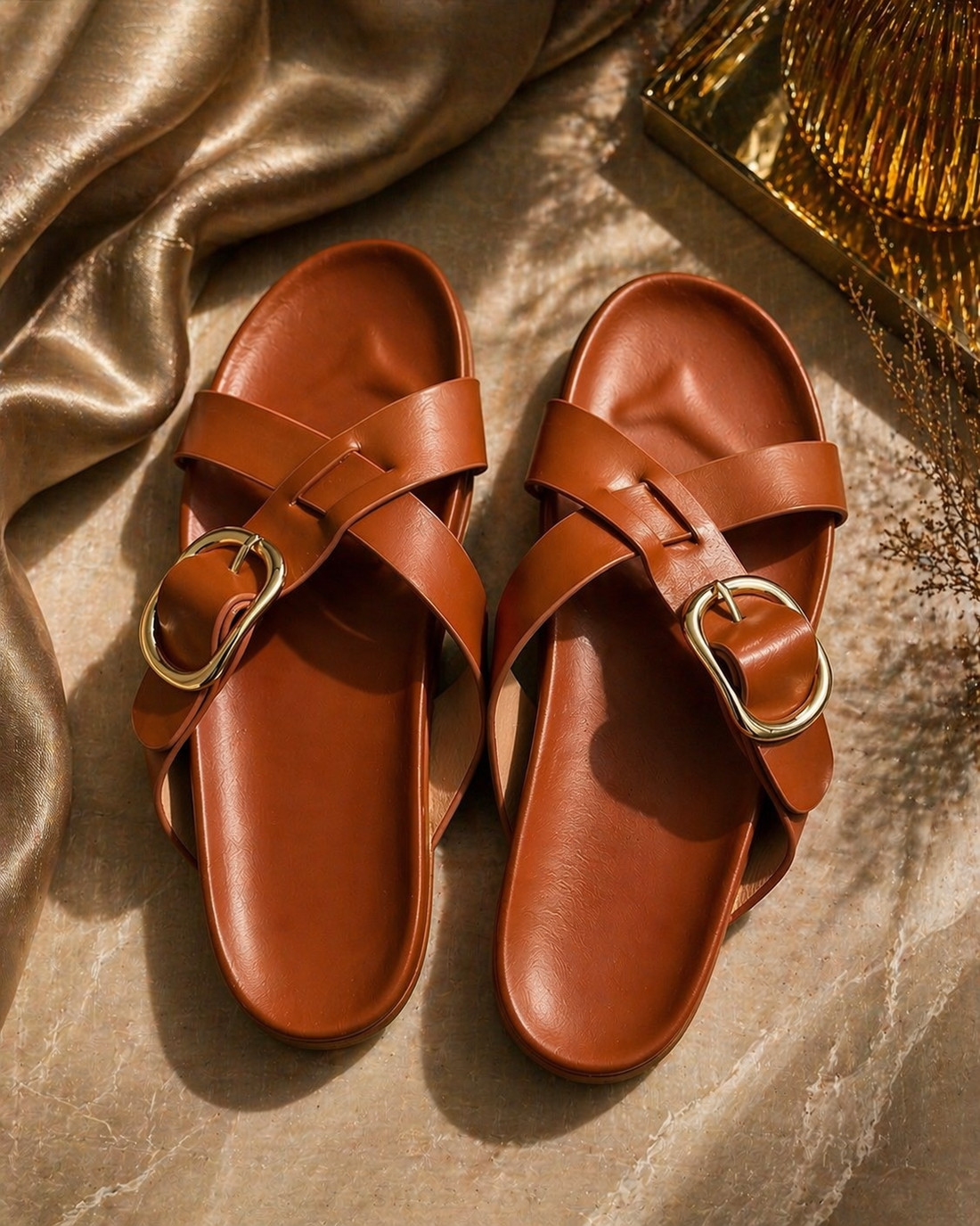 Pair of brown sandals with gold buckles on a textured surface
