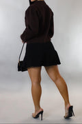 Woman wearing a black outfit with high heels and a handbag on a plain background