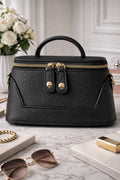 Black handbag with gold accents on a marble surface with sunglasses and a book.