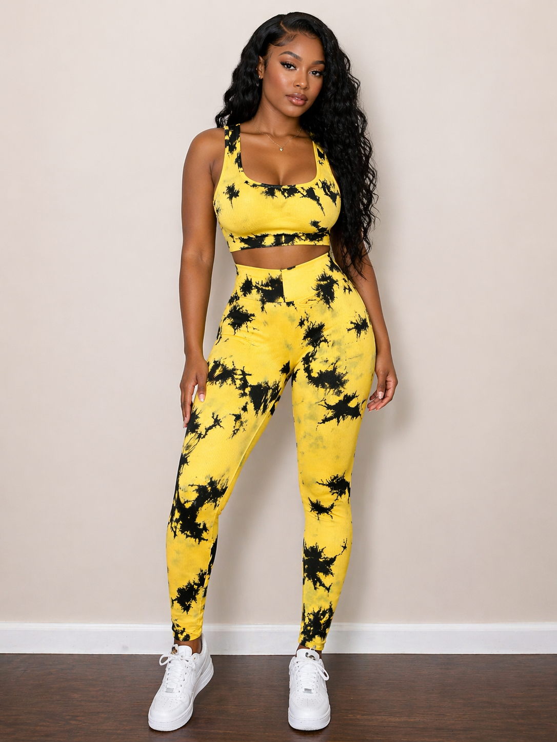 Woman wearing a yellow and black tie-dye outfit against a beige wall.