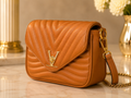 A tan quilted leather shoulder bag with a gold-tone LV logo on the front flap and a gold chain strap, displayed on a marble surface with a blurred background.