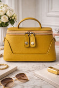 Yellow handbag on a marble surface with sunglasses and a book