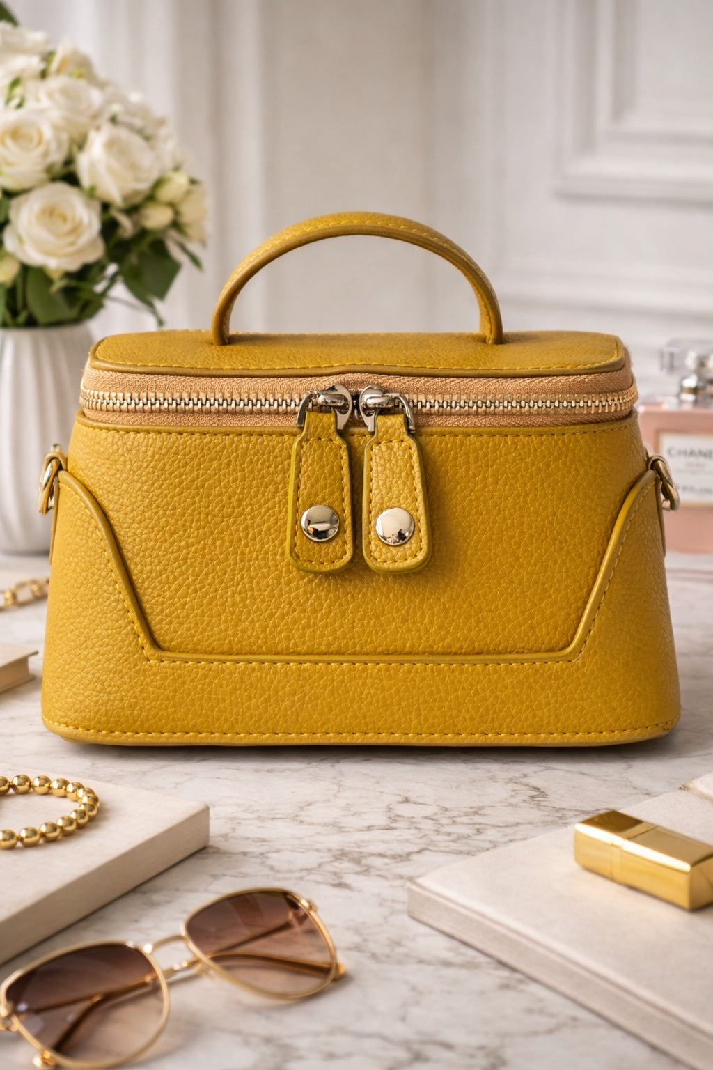 Yellow handbag on a marble surface with sunglasses and a book