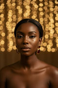 A close-up portrait of a woman with dark skin and black hair pulled back, wearing large gold-toned drop earrings with deep red stones. The background consists of warm, glowing golden bokeh lights.