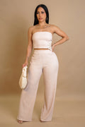 Woman wearing a beige strapless top and wide-leg pants against a beige background