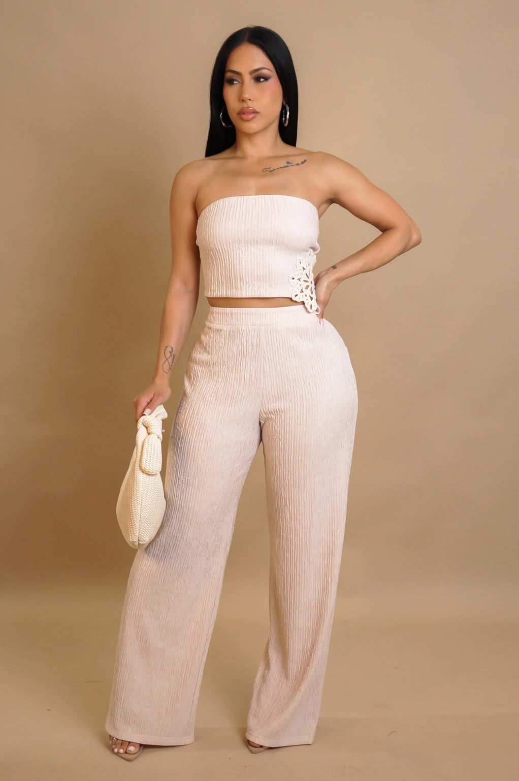 Woman wearing a beige strapless top and wide-leg pants against a beige background