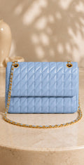 Light blue quilted handbag with gold chain on a beige surface