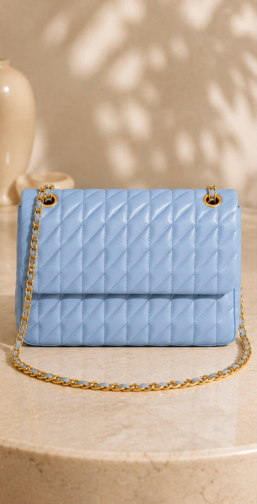 Light blue quilted handbag with gold chain on a beige surface