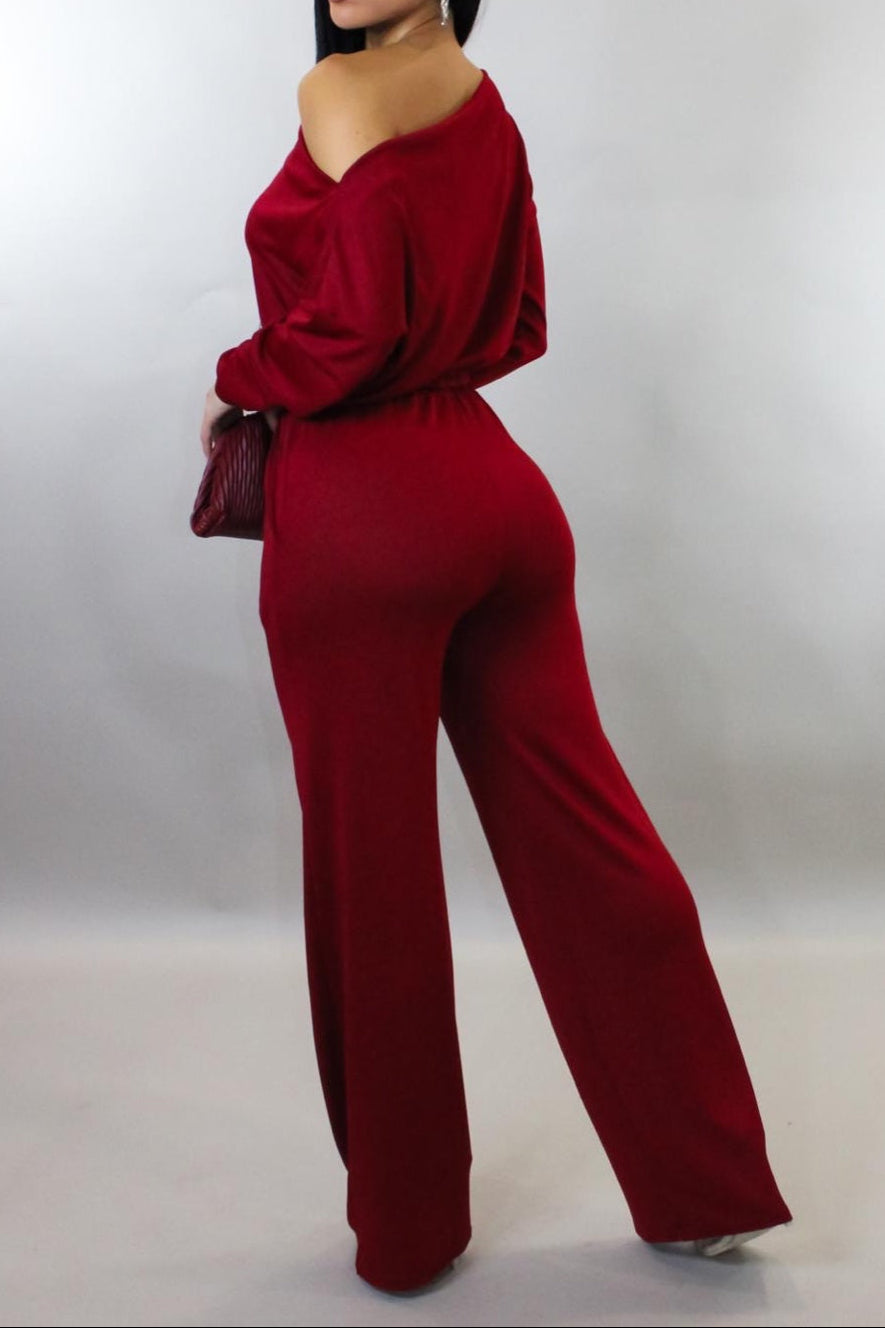 Woman wearing a red jumpsuit holding a matching handbag against a white background