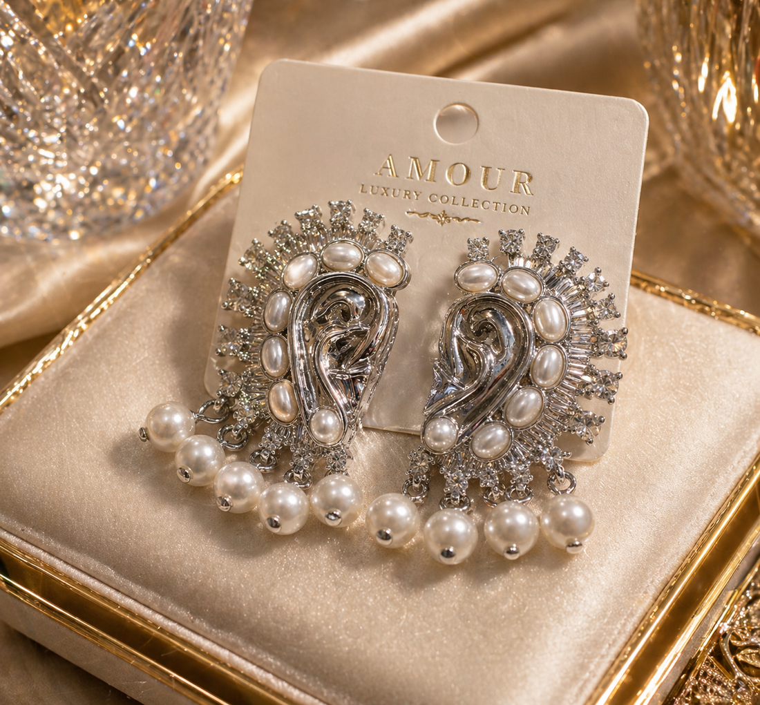 Gold and pearl brooch on a 'AMOUR' branded card with a gold mirror and perfume bottle in the background.