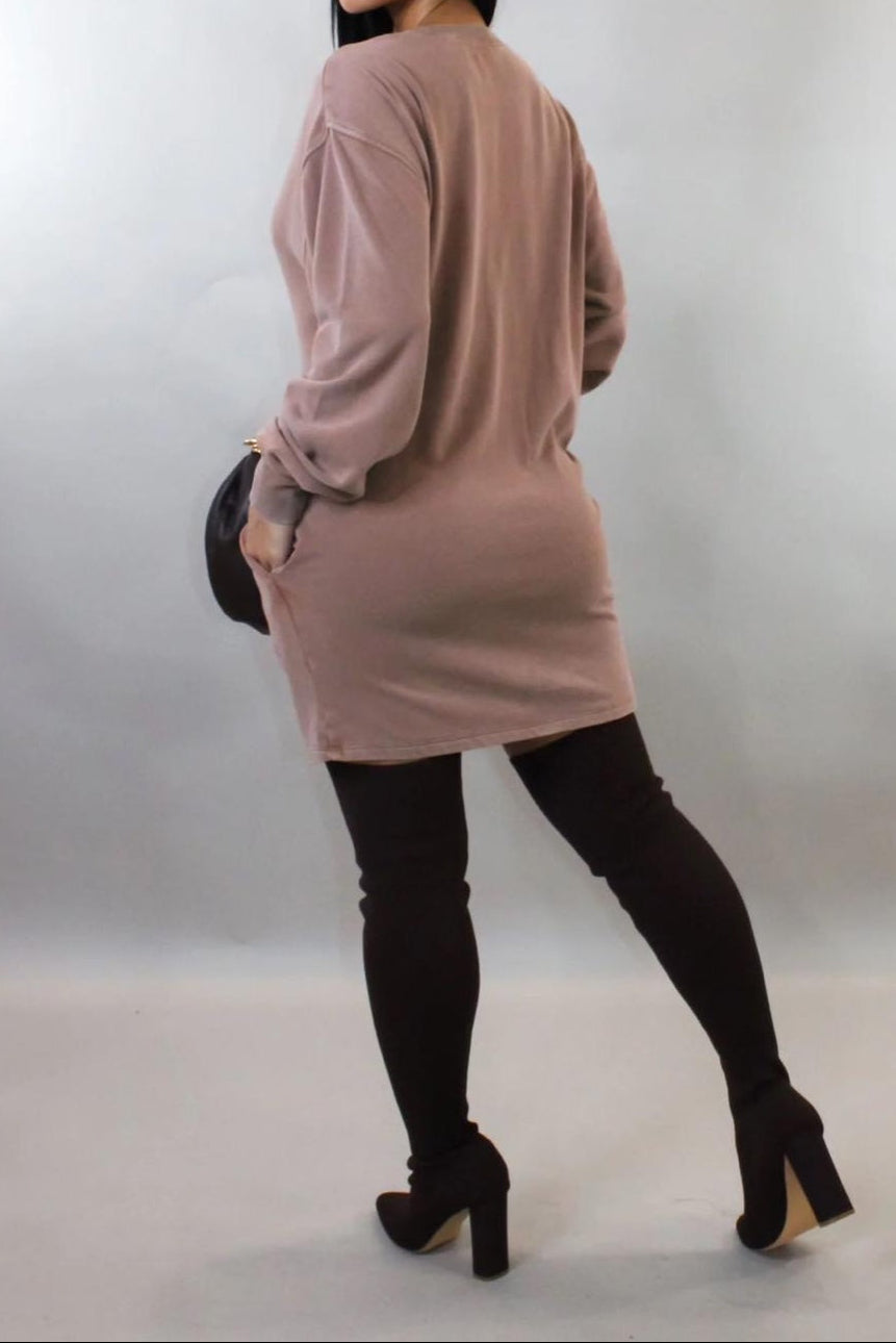 Woman wearing a long beige dress with black leggings and high-heeled shoes on a plain background