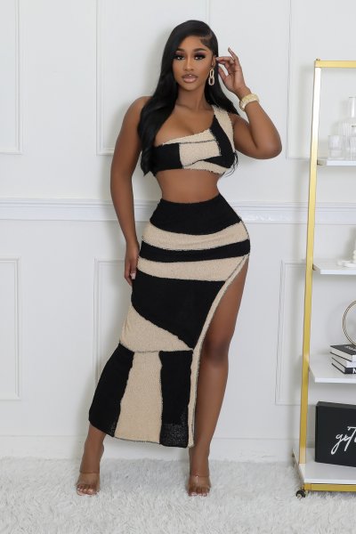 Woman wearing a black and beige striped dress in a room with a white wall and a shelf.