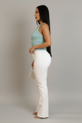 A woman modeling a light blue sleeveless knit top with keyhole cutouts and white high-waisted flare pants, holding a small white woven handbag against a plain gray studio background.