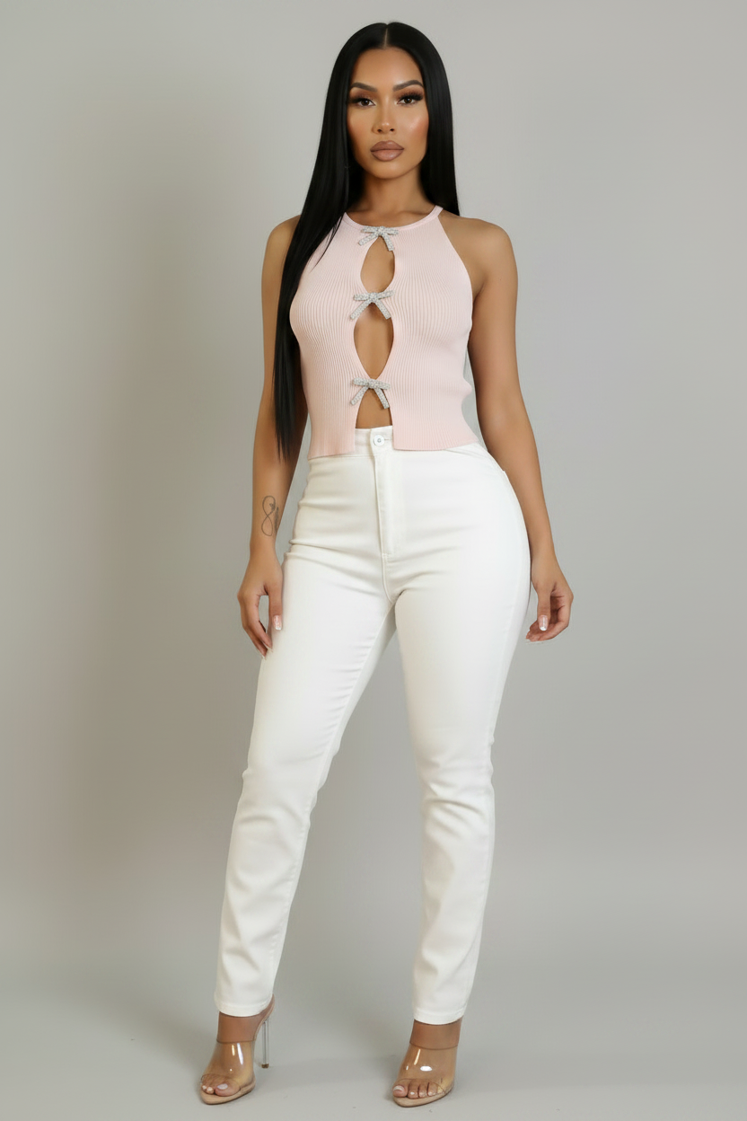 A woman modeling a pale pink ribbed sleeveless top with keyhole cutouts and white pants against a neutral gray studio background.
