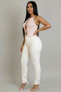 A woman modeling a pale pink sleeveless cutout bodysuit with white skinny jeans and white heeled sandals against a plain light gray studio background.