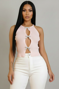 A woman modeling a light pink ribbed halter crop top with three keyhole cutouts and matching bow accents, paired with white pants, against a solid gray studio background.