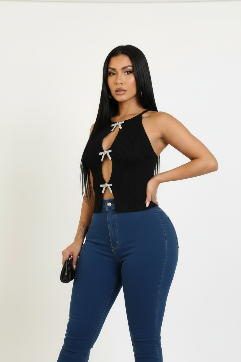 A woman modeling a black halter crop top with silver bow details and blue skinny jeans against a plain white studio background.
