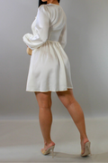 Woman wearing a white dress with long sleeves against a plain background