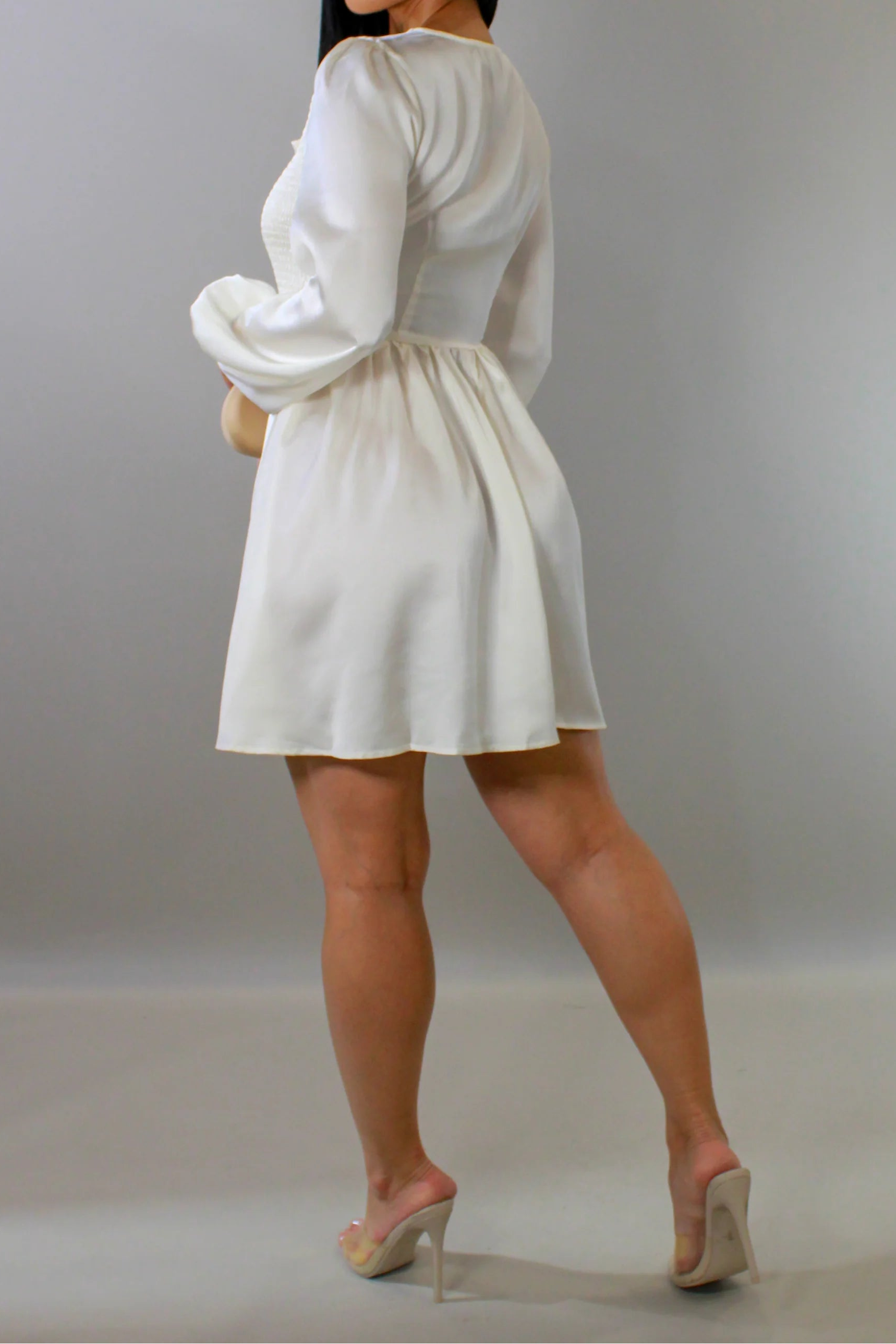 Woman wearing a white dress with long sleeves against a plain background