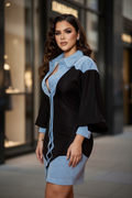 A woman wearing a color-block mini dress with a light blue chambray shirt collar and sleeves, paired with a black body and a matching light blue skirt, standing on a city sidewalk.