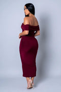 Woman wearing a burgundy off-shoulder dress against a plain background