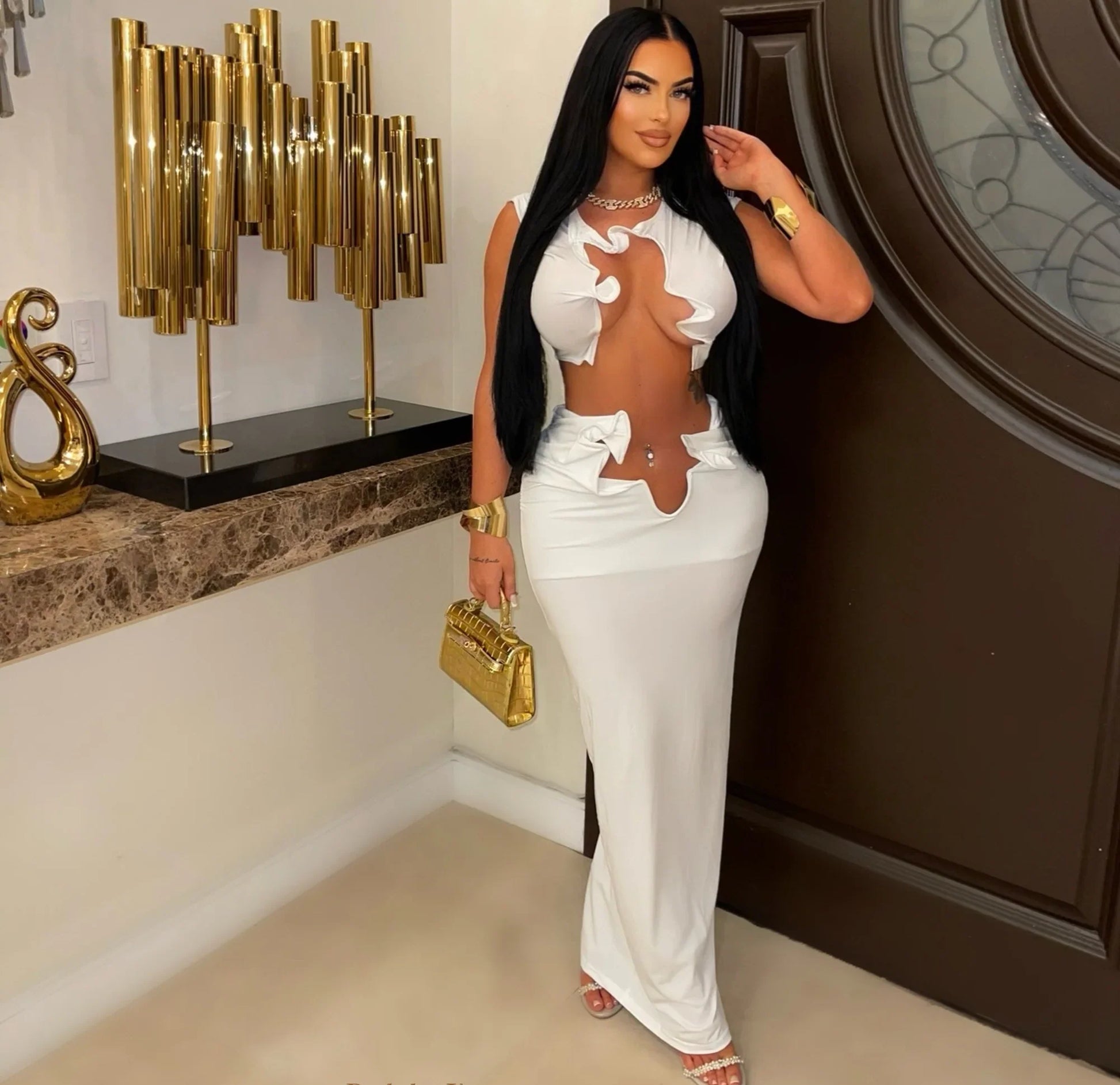 Woman in a white outfit with cut-out design standing in an elegant interior setting.